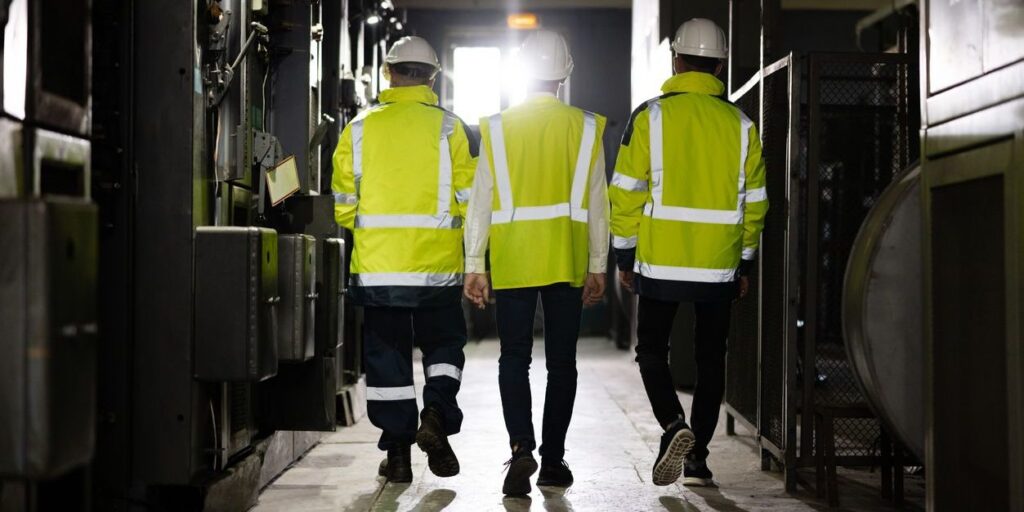 Back view of group team of industrial engineers walking with high visibility vests discussing new project or production plan. Inspectors supervising